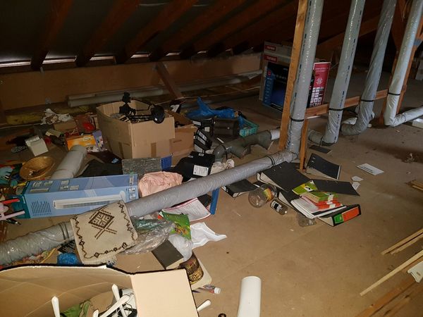Chaotischer Dachboden mit Kartons, Aktenordnern, Rohren und verschiedenen Gegenständen.