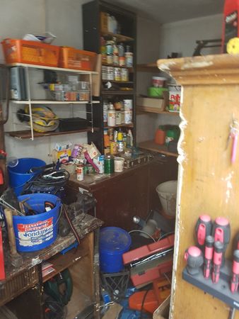 Unordentliche Werkstatt mit Regalen, Werkzeugen, Eimern und verschiedenen Utensilien.