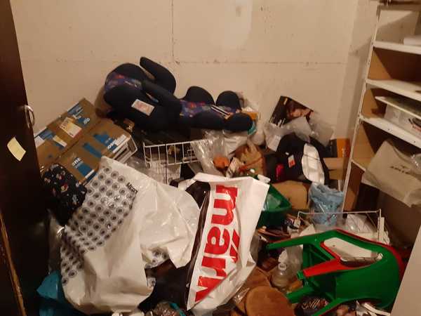 Kellerraum mit Unordnung, gestapelten Kartons, Plastikstühlen, Tüten und Regalen.